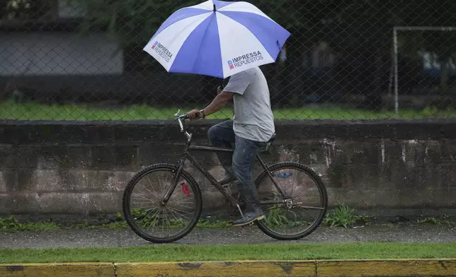 A man rides his bicycle during rains brought on by Tropical Storm Sara in La Lima, Honduras, Friday, Nov. 15, 2024. (AP Photo/Moises Castillo)