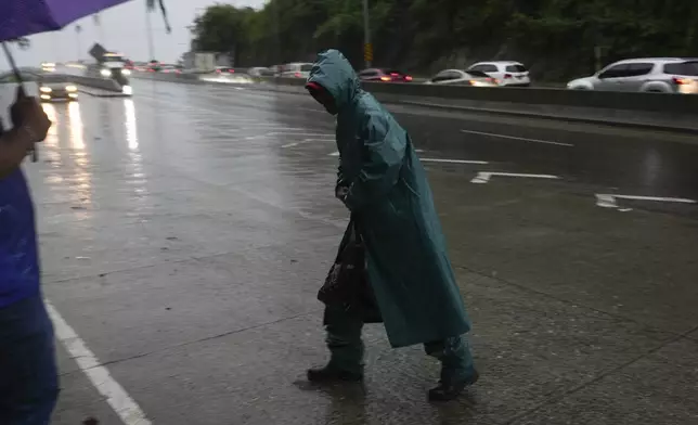 A man walks to his work place during rains brought on by tropical storm Sara in San Pedro Sula, Honduras, Friday, Nov. 15, 2024. (AP Photo/Moises Castillo)