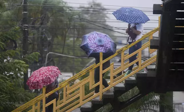 People cross a pedestrian bridge during rains brought on by tropical storm Sara in San Pedro Sula, Honduras, Friday, Nov. 15, 2024. (AP Photo/Moises Castillo)