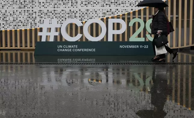 People arrive as it rains at the COP29 U.N. Climate Summit, Monday, Nov. 18, 2024, in Baku, Azerbaijan. (AP Photo/Rafiq Maqbool)