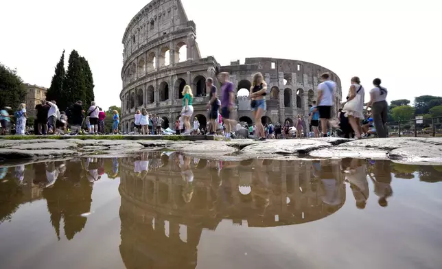 FILE - Tourists walk by the ancient Roman Colosseum as it's reflected in a puddle, in Rome, Sept. 5, 2024. (AP Photo/Andrew Medichini, file)