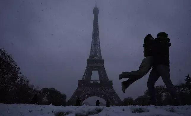 Visitors move as snow falls, with the Eiffel Tower in the background, in Paris, Thursday, Nov. 21, 2024. (AP Photo/Louise Delmotte)