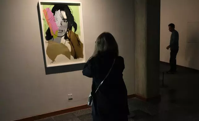 A woman takes a snapshot of a portrait of Rolling Stones frontman Mick Jagger by American artist Andy Warhol as she visits an exhibition titled Eye to Eye which showcases over 120 works by modern world artists as well as Iranian painters at Tehran Museum of Contemporary Art, in Tehran, Thursday, Nov. 21, 2024. (AP Photo/Vahid Salemi)