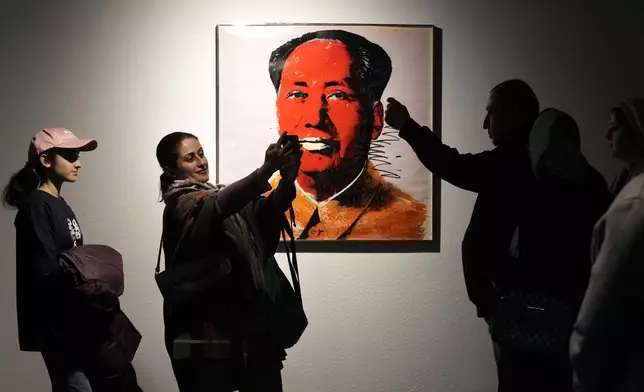 People take snap shots next to China's late leader Mao Zedong painting by American artist Andy Warhol as they visit an exhibition titled Eye to Eye which showcases over 120 works by modern world artists as well as Iranian painters at Tehran Museum of Contemporary Art, in Tehran, Thursday, Nov. 21, 2024. (AP Photo/Vahid Salemi)