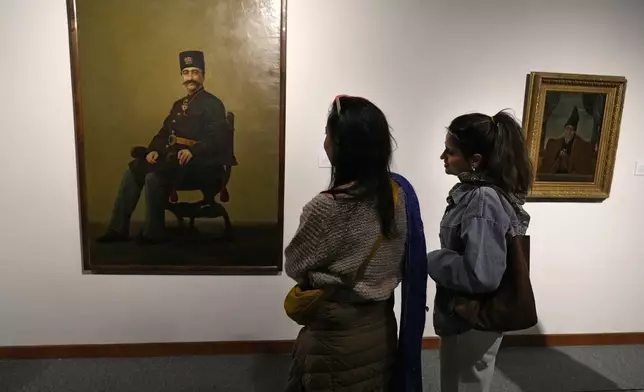 Two women look at a portrait of late Nasser-e-Din Shah, a king of Qajar dynesty, painted by Iranian painter Mohammad Ghaffari, also known as Kamal-ol-Molk, as they visit an exhibition titled Eye to Eye which showcases over 120 works by modern world artists as well as Iranian painters at Tehran Museum of Contemporary Art, in Tehran, Thursday, Nov. 21, 2024. (AP Photo/Vahid Salemi)