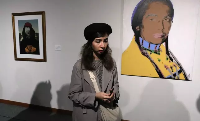 A woman walks past a portrait of the leader of the American Indian Movement Russell Means, right, by American artist Andy Warhol, as she visits an exhibition titled Eye to Eye which showcases over 120 works by modern world artists as well as Iranian painters at Tehran Museum of Contemporary Art, in Tehran, Thursday, Nov. 21, 2024. (AP Photo/Vahid Salemi)