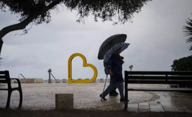 People walk past a sign reading in Hebrew and English "Bring them home now" in reference of the of hostages held in the Gaza Strip by the Hamas militant group, in Haifa, Israel, Tuesday, Nov. 26, 2024. (AP Photo/Francisco Seco)