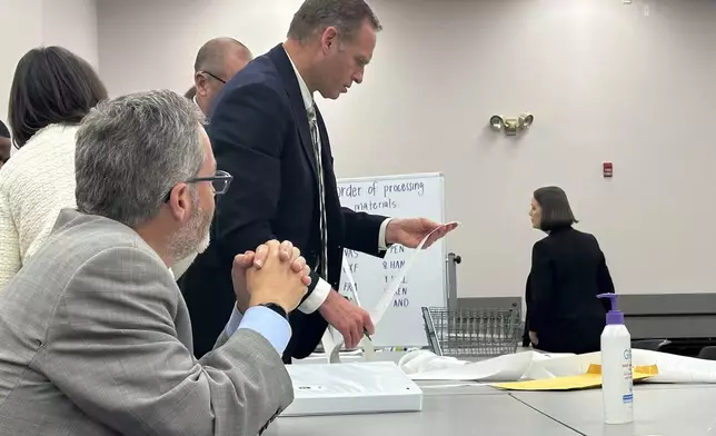 Attorneys and observers review a printout from a voting machine to ensure the numbers match with the reported results as the state conducts additional tabulations under ranked choice voting in a congressional race, Tuesday, Nov. 12, 2024, in Augusta, Maine. (AP Photo/David Sharp)