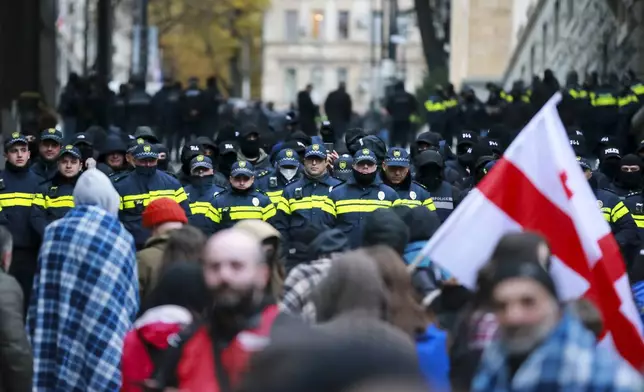 Protesters with a Georgian national flag stand in front of police blocking the entrance of the Parliament's building during a rally to demand new parliamentary elections in the country, in Tbilisi, Georgia, Monday, Nov. 25, 2024. (AP Photo/Zurab Tsertsvadze)