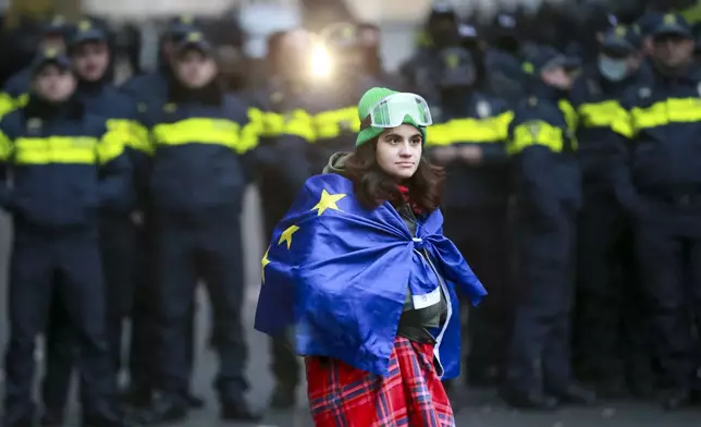 A woman holds an EU flag in front of police blocking the entrance of the Parliament's building during a rally to demand new parliamentary elections in the country, in Tbilisi, Georgia, Monday, Nov. 25, 2024. (AP Photo/Zurab Tsertsvadze)