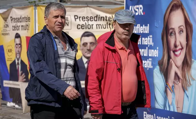 People walk by posters showing candidates in the upcoming Nov. 24 presidential elections, in Bucharest, Romania, Friday, Sept. 20, 2024. (AP Photo/Andreea Alexandru)