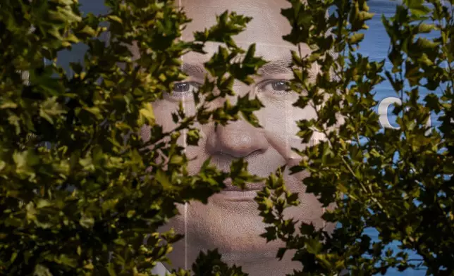 A large poster of Nicolae Ciuca, the National Liberal Party or PNL candidate in the upcoming Nov. 24 presidential elections, peers from behind trees in Bucharest, Romania, Friday, Sept. 20, 2024. (AP Photo/Vadim Ghirda)