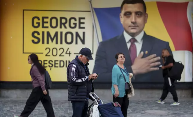 People wallk outside the electoral campaign headquarters of George Simion, the Alliance for the Unity of Romanians or AUR candidate in the upcoming Nov. 24 presidential elections, in Bucharest, Romania, Friday, Sept. 20, 2024. (AP Photo/Vadim Ghirda)