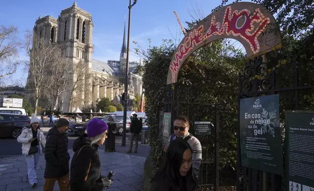 People enter a Christmas market as French President Emmanuel Macron visits the renovated Notre Dame Cathedral Friday, Nov. 29, 2024 in Paris. (AP Photo/Michel Euler)