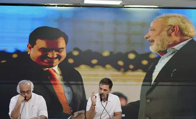 India's opposition Congress party leader Rahul Gandhi, center, addresses the media on Indian businessman Gautam Adani, after Adani was indicted by U.S. prosecutors on charges he duped investors in a massive solar energy project in India, in New Delhi, India, Thursday, Nov. 21, 2024. Image behind shows Adani, on left with Indian Prime Minister Narendra Modi, on right. (AP Photo/Manish Swarup)