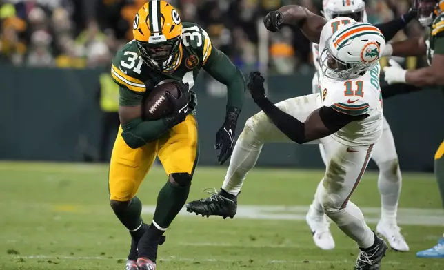 Green Bay Packers running back Emanuel Wilson (31) runs from Miami Dolphins linebacker Tyrel Dodson (11) during the first half of an NFL football game Thursday, Nov. 28, 2024, in Green Bay, Wis. (AP Photo/Morry Gash)