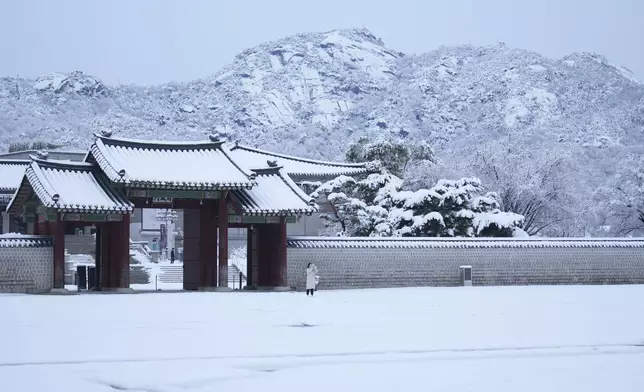 A visitor holds her smartphone outside of the snow-covered National Palace Museum in Seoul, South Korea, Wednesday, Nov. 27, 2024. (AP Photo/Lee Jin-man)