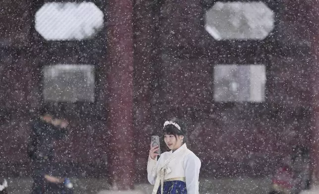 Chan Yian from Taiwan holds her smartphone in snow at the Gyeongbok Palace, one of South Korea's well-known landmarks, in Seoul, South Korea, Wednesday, Nov. 27, 2024. (AP Photo/Lee Jin-man)