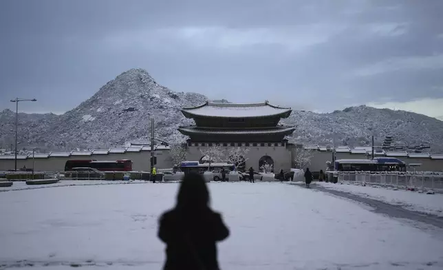 A pedestrian stops to take photo the snow-covered Gwanghwamun, the main gate of the 14th-century Gyeongbok Palace, one of South Korea's well known landmarks, in Seoul, South Korea, Wednesday, Nov. 27, 2024. (AP Photo/Lee Jin-man)