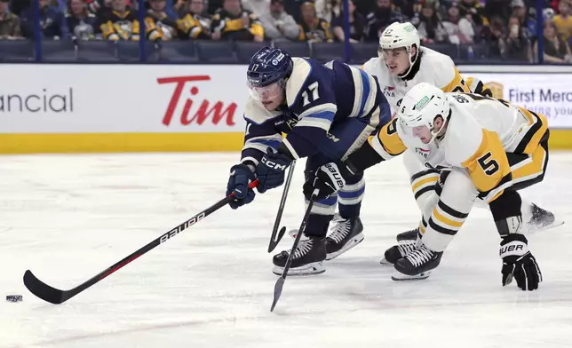 Columbus Blue Jackets forward Justin Danforth, left, reaches for the puck in front of Pittsburgh Penguins defenseman Ryan Graves, center, and defenseman Ryan Shea during the second period of an NHL hockey game in Columbus, Ohio, Friday, Nov. 15, 2024. (AP Photo/Paul Vernon)