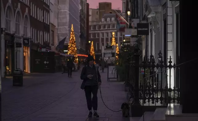 A woman walks a dog in a street of Mayfair at sunrise, in London, Friday, Nov. 29, 2024.(AP Photo/Alberto Pezzali)