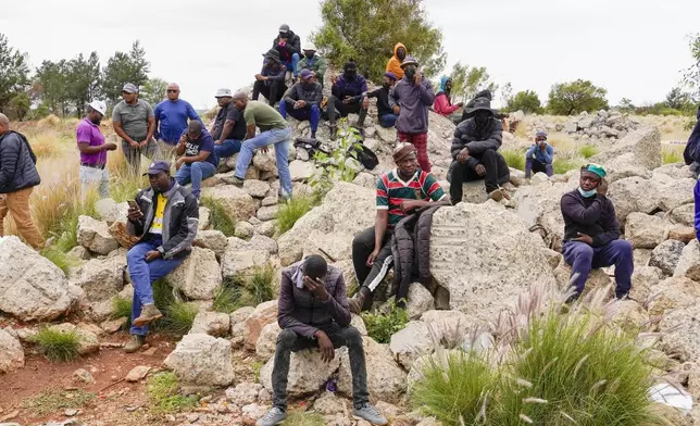 Volunteer rescuers sit by the opening of a reformed gold mineshaft where illegal miners are trapped in Stilfontein, South Africa, Friday, Nov. 15, 2024. (AP Photo/Denis Farrell)