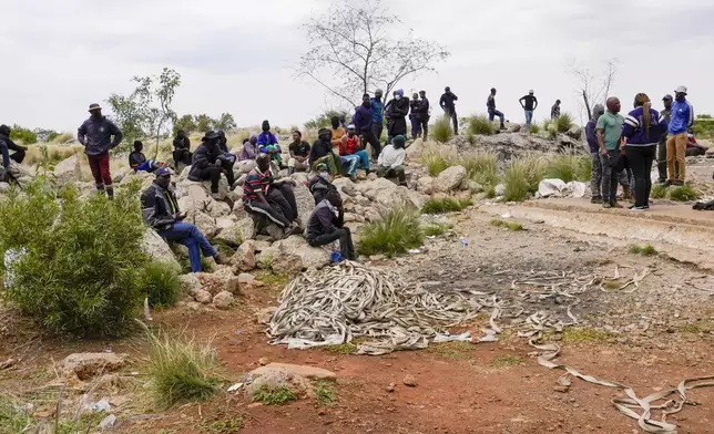 Volunteer rescuers sit by the opening of a reformed gold mineshaft where illegal miners are trapped in Stilfontein, South Africa, Friday, Nov. 15, 2024. (AP Photo/Denis Farrell)