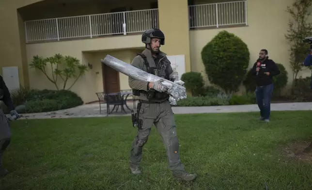 An Israeli bomb squad police officer carries the remains of a rocket that was fired from Lebanon in Kibbutz Kfar Blum, northern Israel Sunday Nov. 24, 2024. (AP Photo/Ohad Zwigenberg)