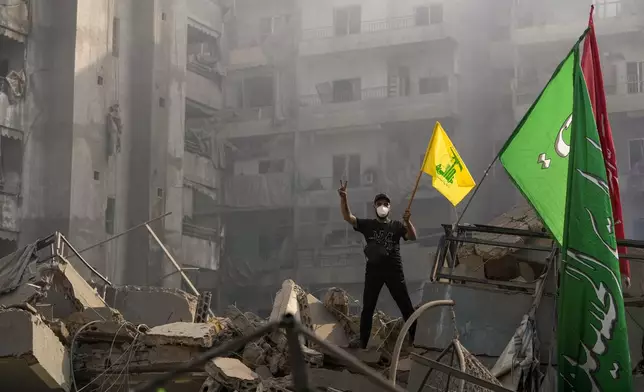 FILE - A man flashes the victory sign as he holds up a Hezbollah flag while standing on the ruins of his apartment after an Israeli airstrike in Dahiyeh, Beirut, Lebanon, on Nov. 1, 2024. (AP Photo/Hassan Ammar, File)