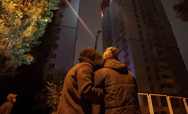 A couple comforts each other while looking at the fire in a residential building after the attack of Russian drones in Kyiv, Ukraine, Friday, Oct. 26, 2024. (AP Photo/Alex Babenko)