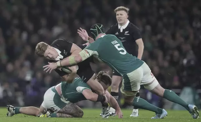 New Zealand's Jordie Barrett, center, is tackled by Ireland's Finlay Bealham, left, and James Ryan (5) during the Autumn international rugby match, Friday, Nov. 8, 2024, at Aviva Stadium in Dublin, Ireland. (Brian Lawless/PA via AP)