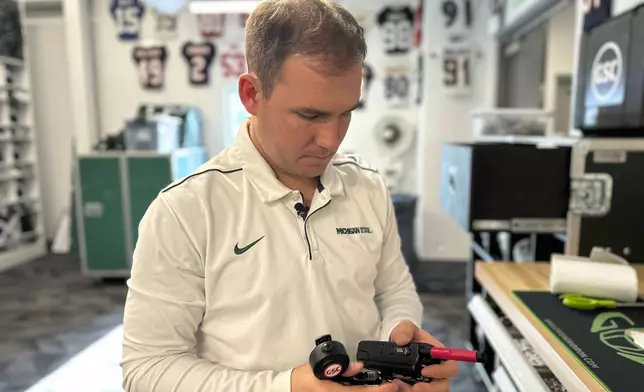 Andrew Kolpacki, Michigan State University's head football equipment manager, examines part of a coach-to-player communication system inside the school's football complex, Monday, Nov. 18, 2024, in East Lansing, Mich. (AP Photo/Mike Householder)