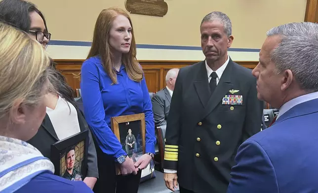 FILE - Amber Sax, center, holds a photo of her late husband, Marine Corps MV-22B pilot Capt. John Sax, as she and other family members who have lost service members to Osprey crashes talk with Vice Adm. Carl Chebi, Commander of U.S. Naval Air Systems Command, center right, and Peter Belk, acting Assistant Secretary of Defense for Readiness, right, before a hearing on the programs safety record, Wednesday, June 12, 2024, on Capitol Hill in Washington. (AP Photo/Tara Copp)