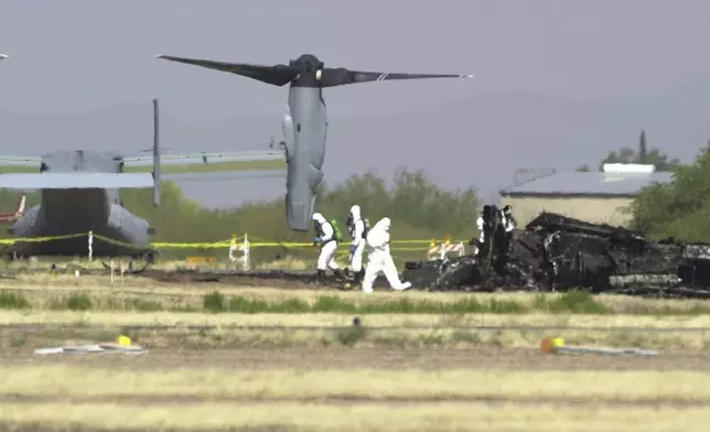 FILE - White suited workers investigate the crash scene of a Marine Corps MV-22 Osprey at the Avra Valley Airport, north of Tucson, Ariz., April 9, 2000. A Marine Corps aircraft attempting to land during a nighttime training mission crashed and burst into flames, killing all 19 aboard and adding to a checkered history for a new breed of hybrid plane that can take off and land like a helicopter. (AP Photo/Jon Hayt, File)