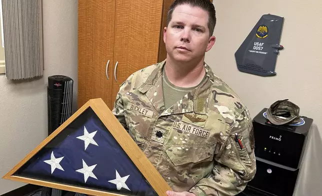 Lt. Col. Seth Buckley, an Osprey squadron commander at Cannon Air Force Base, N.M., who lost his brother in an Air Force Special Operations Command MC-130H crash (AFSOC) when he was still in high school, poses for a photo in his office Oct. 8, 2024.. Buckley says, "I think my job here is to ensure that I'm going to push it to the level that we are making sure we aren't delivering any more of these," he said of the flag the Air Force gave his family, which he keeps in his office. (AP Photo/Tara Copp)