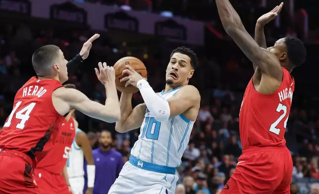 Charlotte Hornets guard Josh Green (10) drives between Miami Heat guard Tyler Herro (14) and forward Haywood Highsmith during the first half of an NBA basketball game in Charlotte, N.C., Wednesday, Nov. 27, 2024. (AP Photo/Nell Redmond)