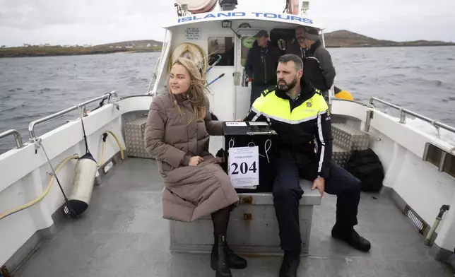 Presiding officer Caroline Sharkey and Garda Ronan Steede look after a ballot box that is taken by boat to the Island of Gola as voters go to polls the for the 2024 General Election in Ireland, Friday, Nov. 29, 2024. (AP Photo/Peter Morrison)