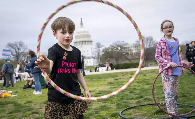 FILE - Mac Gordon Frith, 6, left, who is here supporting his sibling, Caleta Frith, 9, right, who is non-binary, plays with a hula hoop during a rally on the Transgender Day of Visibility, Friday, March 31, 2023, by the Capitol in Washington. (AP Photo/Jacquelyn Martin, File)