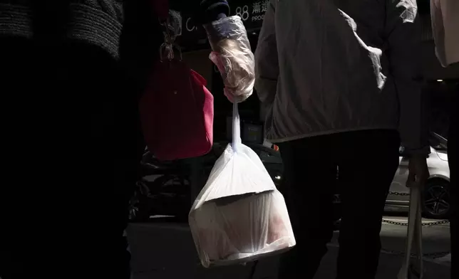 FILE - A pedestrian carries takeaway food in a plastic bag in Hong Kong, March 13, 2024.(AP Photo/Louise Delmotte, File)