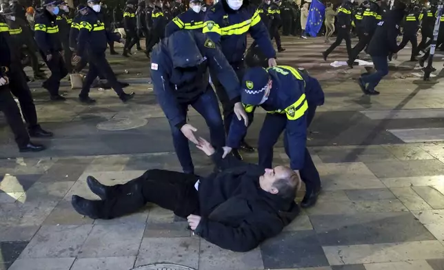 Police officers help a man get up as they push protesters away after destroying a tent camp on a street during a rally against the results of the parliamentary elections amid allegations that the vote was rigged in Tbilisi, Georgia, Tuesday, Nov. 19, 2024. (AP Photo/Zurab Tsertsvadze)