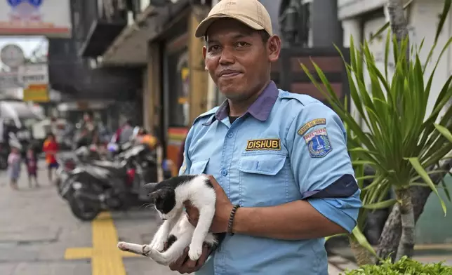 Alvin, a parking attendant, holds Hitam, a stray cat he's been looking after, after it was returned by volunteers during a "Trap, Neuter and Return" project aimed at reducing stray cat population, in Jakarta, Indonesia, on Nov. 12, 2024. (AP Photo/Dita Alangkara)