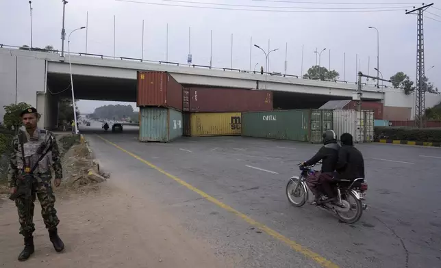 A paramilitary soldier stands guard as a motorcyclist drives on a highway, which partially closed with shipping containers ahead of a planned rally by supporters of imprisoned former Prime Minister Imran Khan's Pakistan Tehreek-e-Insaf party, in Islamabad, Pakistan, Saturday, Nov. 23, 2024. (AP Photo/Anjum Naveed)