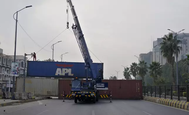 Workers place shipping containers to close a road ahead of a planned rally by supporters of imprisoned former Prime Minister Imran Khan's Pakistan Tehreek-e-Insaf party, in Islamabad, Pakistan, Saturday, Nov. 23, 2024. (AP Photo/Anjum Naveed)