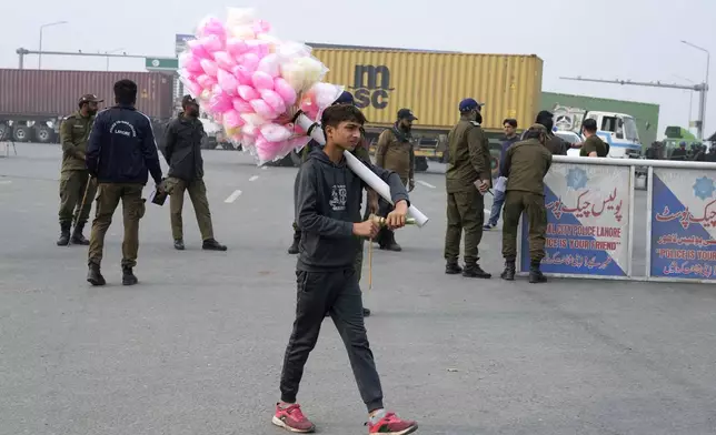 A cotton-candy seller walks past police officers stand guard on an entry point to motorway leading to Islamabad, which has been closed by authorities due to a planned rally by supporters of imprisoned former Prime Minister Imran Khan's Pakistan Tehreek-e-Insaf party, in Lahore, Pakistan, Saturday, Nov. 23, 2024. (AP Photo/K.M. Chaudary)