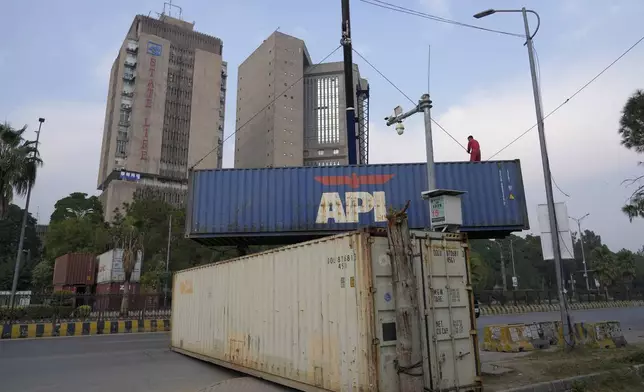 A worker places shipping containers to close a road ahead of a planned rally by supporters of imprisoned former Prime Minister Imran Khan's Pakistan Tehreek-e-Insaf party, in Islamabad, Pakistan, Saturday, Nov. 23, 2024. (AP Photo/Anjum Naveed)