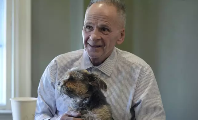 Michael Sullivan, 64, of Lowell, Mass., who was convicted of murder and armed robbery in 1987 and spend years in jail before being ruled innocent, holds his six-year-old Yorkshire terrier "Buddy" while speaking with a reporter from The Associated Press at his attorney's office, Wednesday, Nov. 20, 2024, in Framingham, Mass. (AP Photo/Steven Senne)