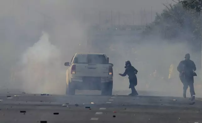 Supporters of imprisoned former Premier Imran Khan's Pakistan Tehreek-e-Insaf party run for cover as police fire tear gas shells to disperse them during clashes in Islamabad, Pakistan, Tuesday, Nov. 26, 2024. (AP Photo/Anjum Naveed)