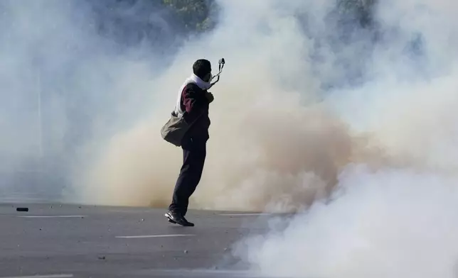 A police officer aims to throw stone with a slingshot after others fire tear gas shells to disperse supporters of imprisoned former Premier Imran Khan's Pakistan Tehreek-e-Insaf party, during clashes in Islamabad, Pakistan, Tuesday, Nov. 26, 2024. (AP Photo/Anjum Naveed)