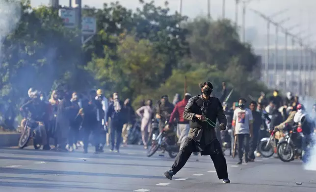 Supporters of imprisoned former premier Imran Khan's Pakistan Tehreek-e-Insaf party, aim to throw stones with slingshot following police fire tear gas shell to disperse them during clashes, in Islamabad, Pakistan, Tuesday, Nov. 26, 2024. (AP Photo/Anjum Naveed)