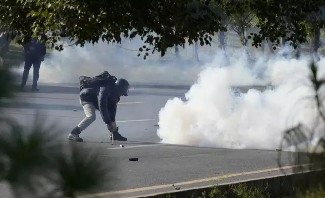 A police officer removes a tear gas shell thrown back by supporters of imprisoned former premier Imran Khan's Pakistan Tehreek-e-Insaf party, during clashes, in Islamabad, Pakistan, Tuesday, Nov. 26, 2024. (AP Photo/Anjum Naveed)